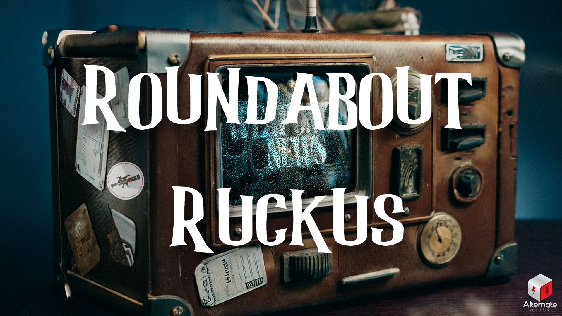 A vintage looking television screen embedded into a brown leather rectangular box that looks like a piece of luggage, with a brown and metallic frame, covered in worn stickers and labels. The screen displays static, and the front panel includes retro dials and switches.