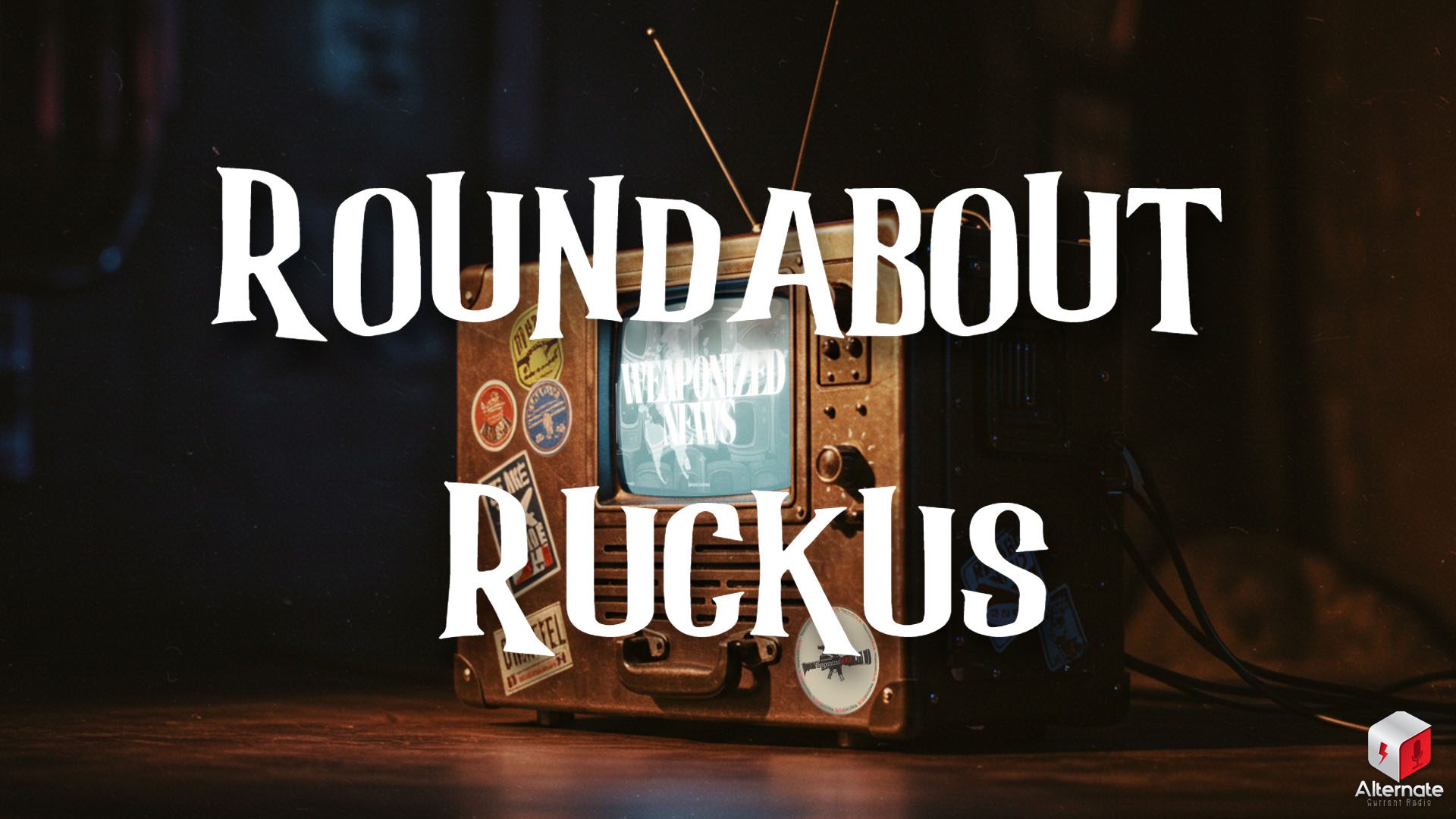 A vintage television set sits on a dark surface in a dimly lit environment. The TV has a boxy design with analog knobs, a speaker grill, a carrying handle on the front, and two antennae extending from the top. The casing is covered in colorful stickers. The screen displays a black-and-white image with the text “WEAPONIZED NEWS” in bold, stylized letters.